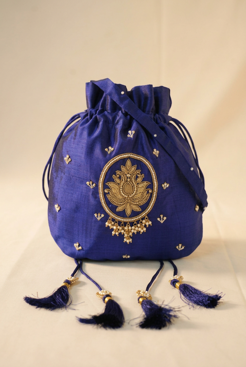 A royal blue drawstring pouch bag with gold embroidery and tassel details, set against a neutral cream background.