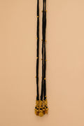 A long black velvet necklace with gold bead accents and a gold-toned coin pendant, hanging on a beige wall next to a white door frame.